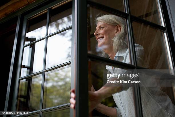 mature woman in window, smiling, low angle view - lüften stock-fotos und bilder