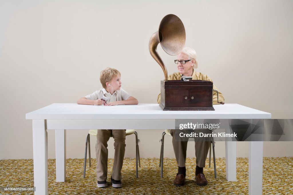 Boy (10-11) with mp3 player and man with gramophone sitting at table