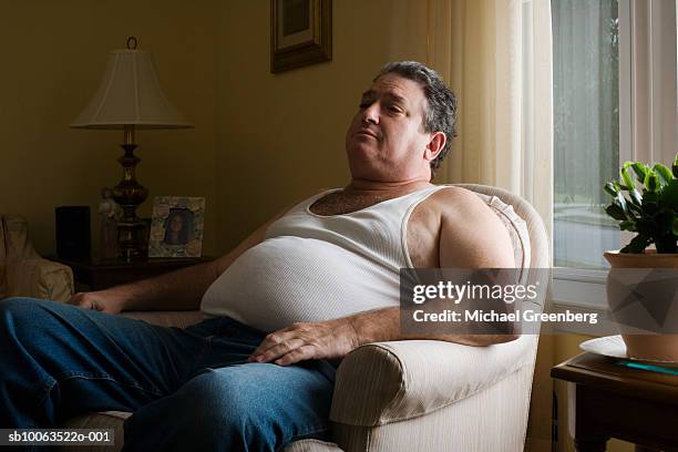 mature overweight man sitting in armchair - couch potato stock-fotos und bilder