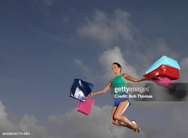 smiling woman carrying bags jumping, low angle view - sportswear shopping stock-fotos und bilder