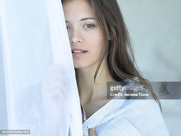 young woman peering through curtains, smiling - persona attraente foto e immagini stock