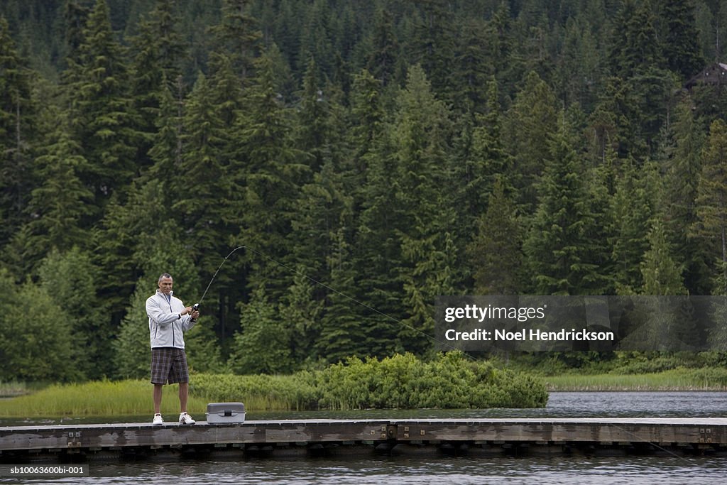 Mature man in distance, fishing from pier, forest in background