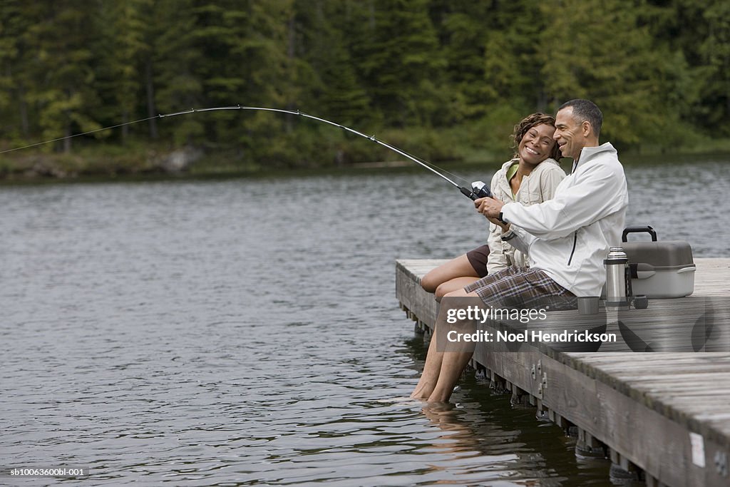 Mature Couple Sitting On Pier Man Fishing Side View High-Res Stock
