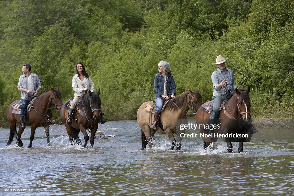 Four horse riders crossing river, forest in background