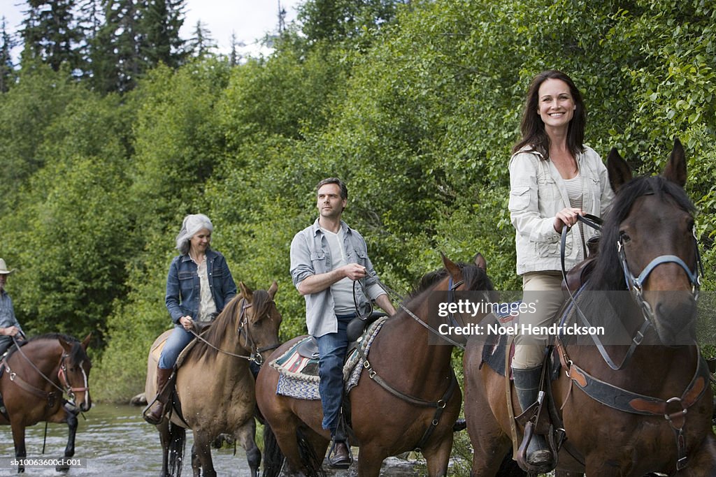 Group of four horse riders crossing river, woman looking at camera