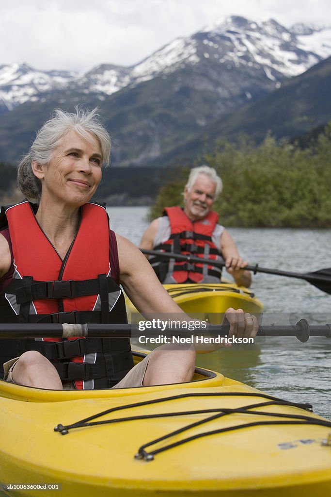 Man and woman in kayaks, wearing life jackets, mountain range in background