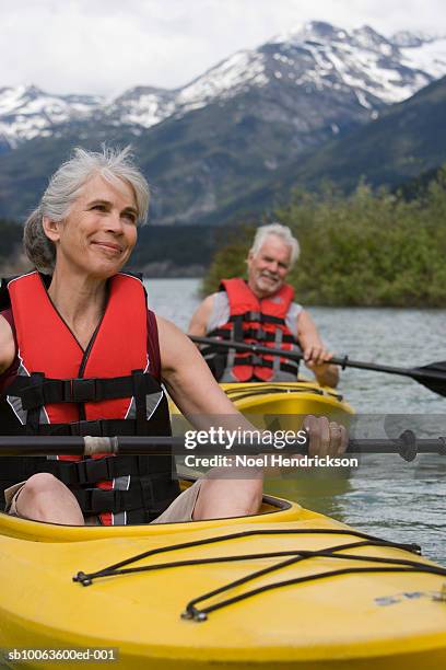 man and woman in kayaks, wearing life jackets, mountain range in background - mountain range stock pictures, royalty-free photos & images