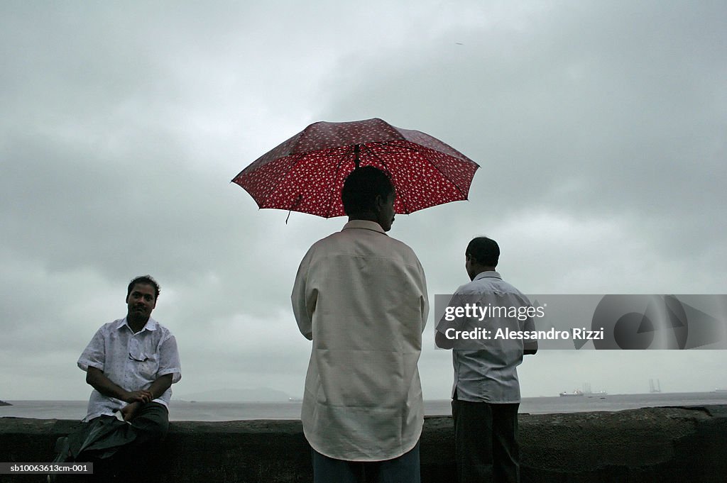 Three men, one with umbrella at promenade