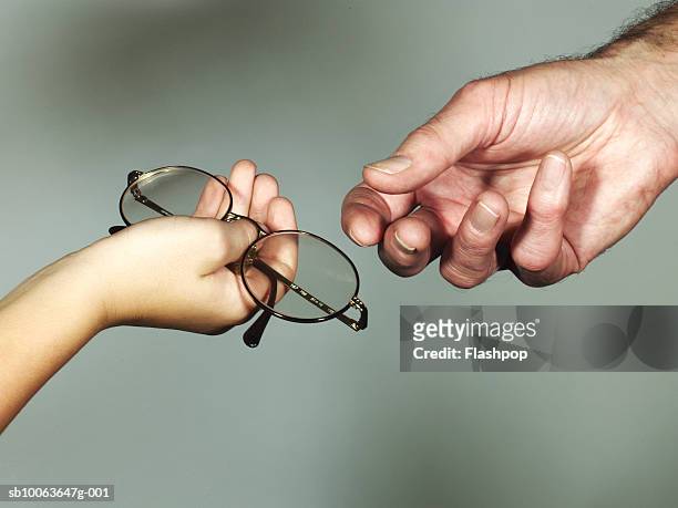 grandson (6-7) giving spectacles to grandfather, close-up - eyewear stock-fotos und bilder