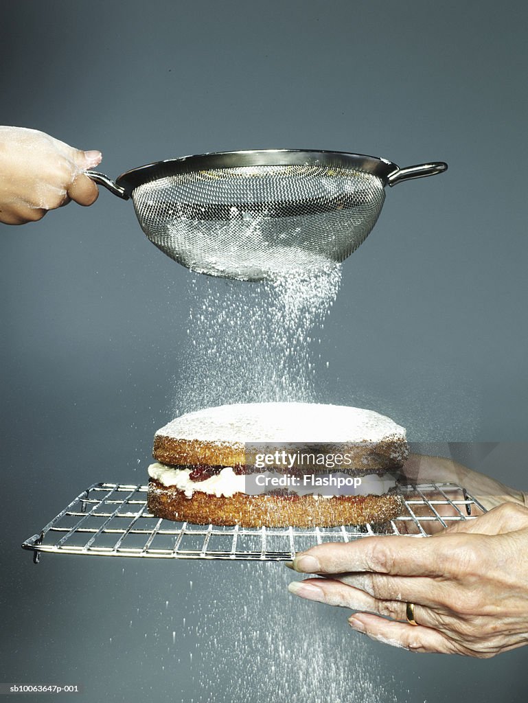 Grandmother holding cake granddaughter (6-7) sieving sugar, close-up