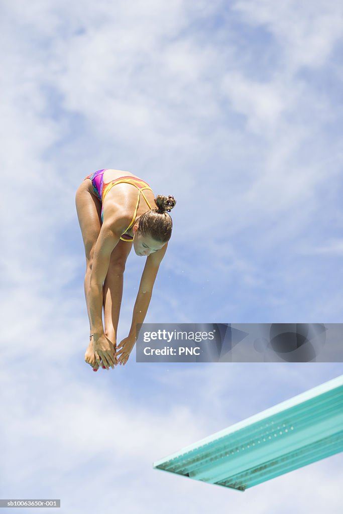 Young woman jumping from diving board, low angle view