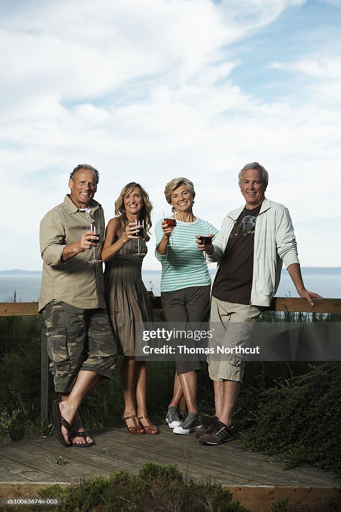 Two mature couples standing in garden holding drinks, smiling