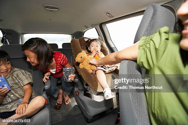 mother handing toy to children (1-10) travelling in car - kid car seat stock pictures, royalty-free photos & images