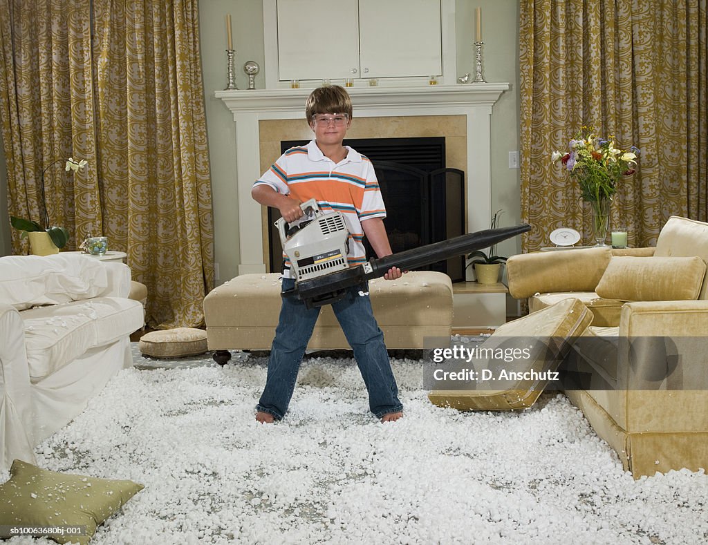 Boy (10-11) holding leaf blower standing in pile of packing peanut in living room, portrait