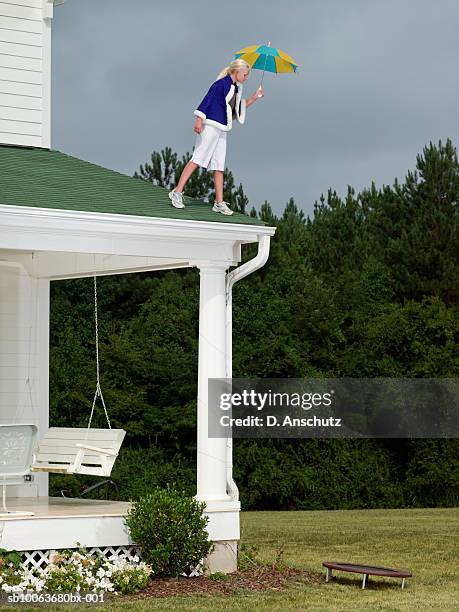 girl (10-11) wearing cape and holding umbrella, preparing to jump off roof of house onto small trampoline - superwoman stockfoto's en -beelden