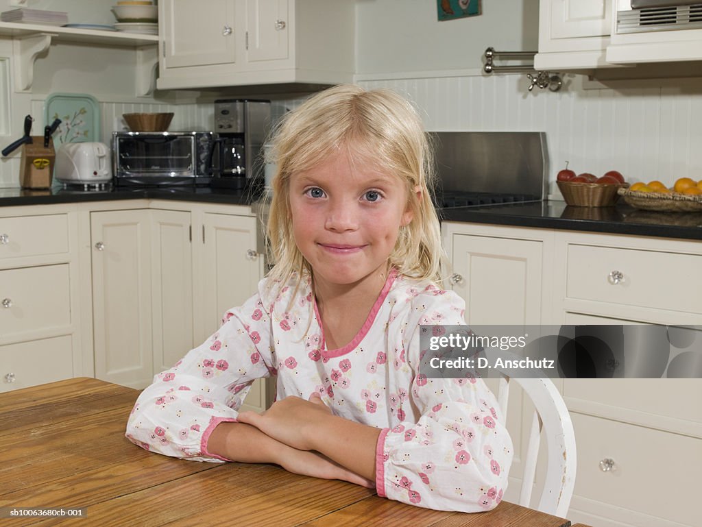 Girl (8-9) in pajamas sitting at kitchen table