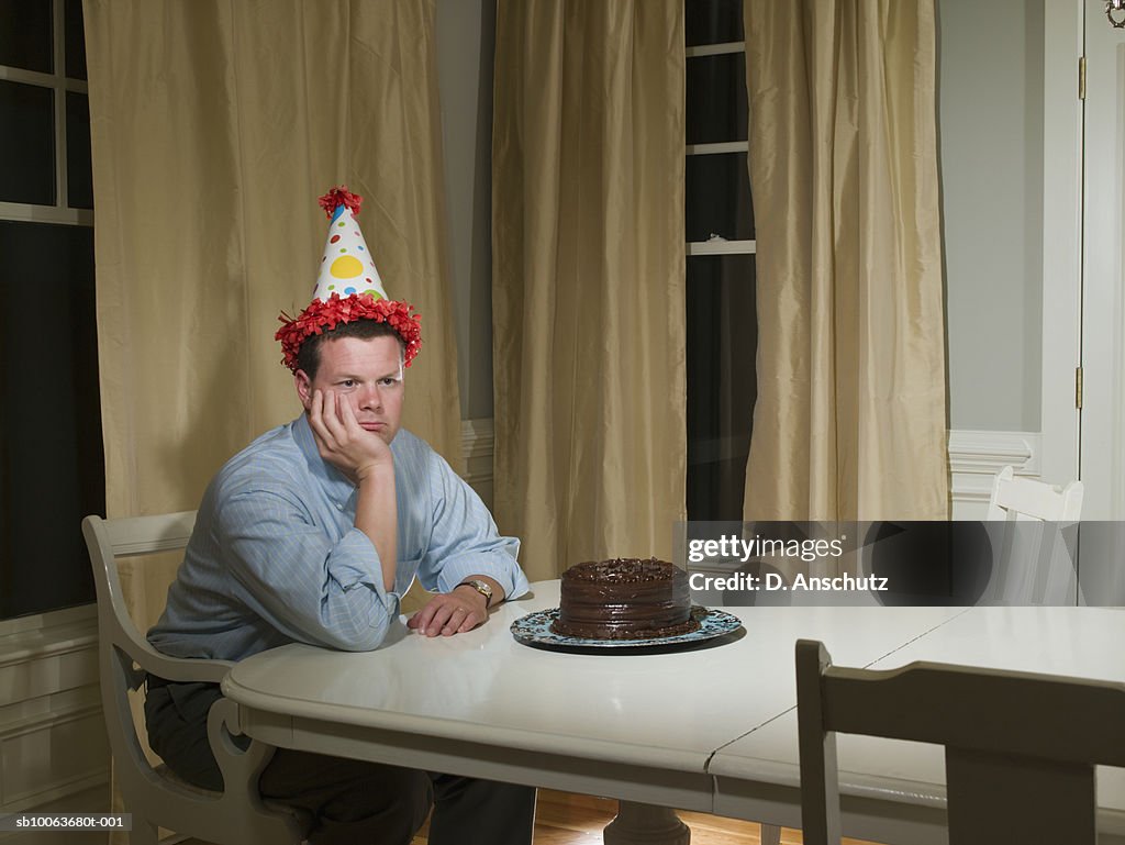 Mid adult man in party hat, sitting at table in front of birthday cake