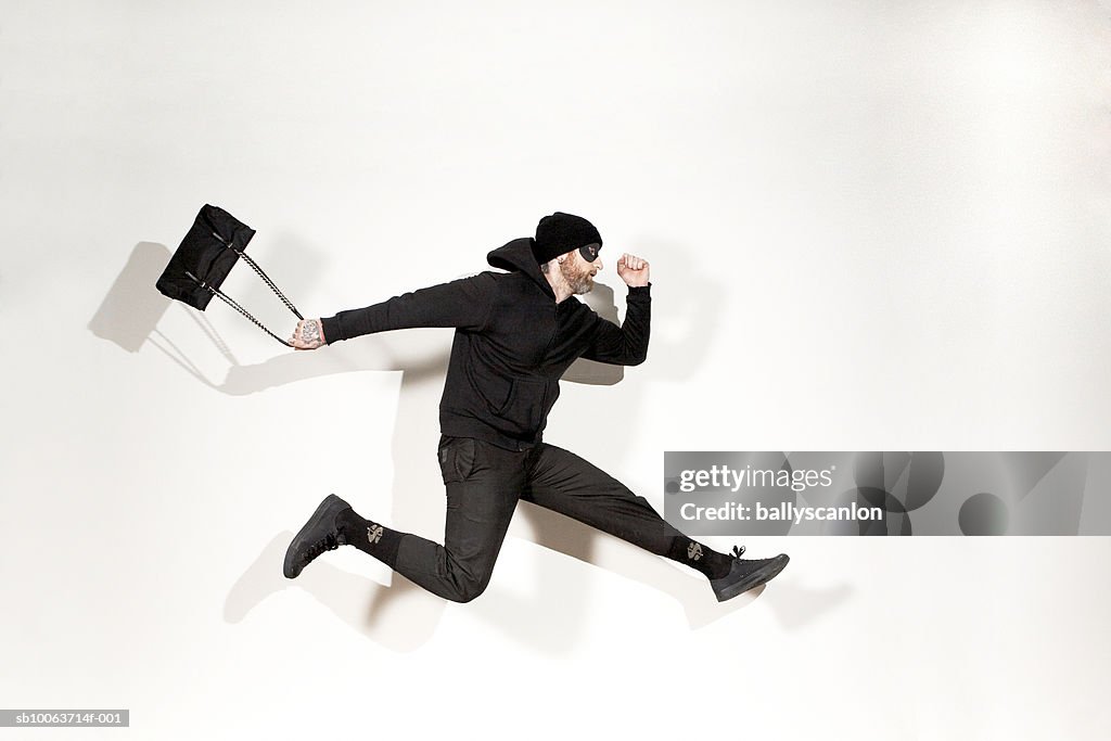 Man running mid-air with handbag, side view