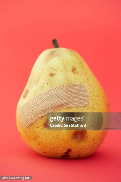 bruised pear with band-aid on red background - prellung stock-fotos und bilder