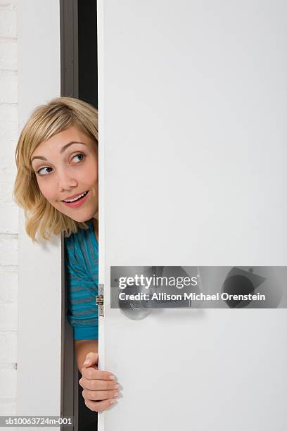 young woman peering through doorway, smiling - peeking stock-fotos und bilder