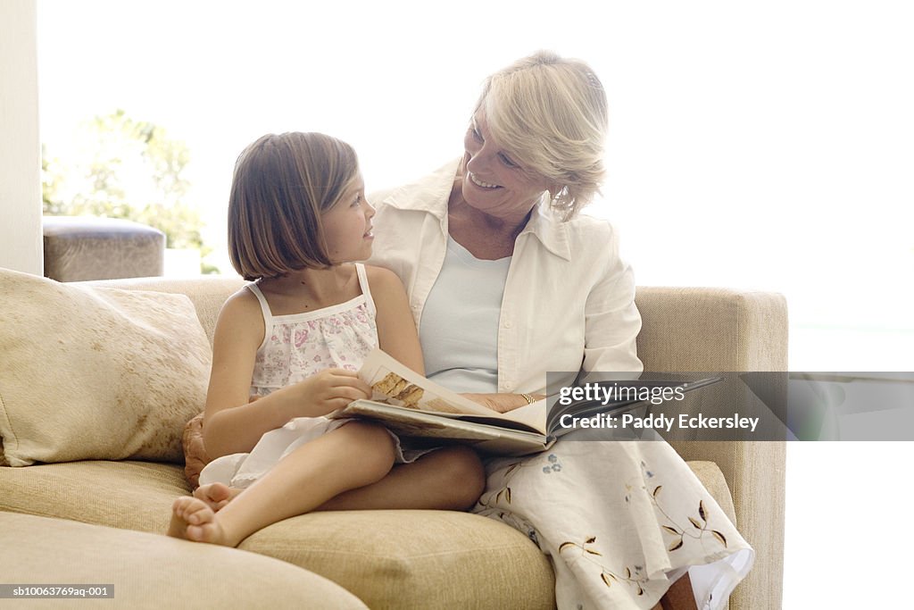 Senior woman with granddaughter (8-9) sitting on sofa, reading book
