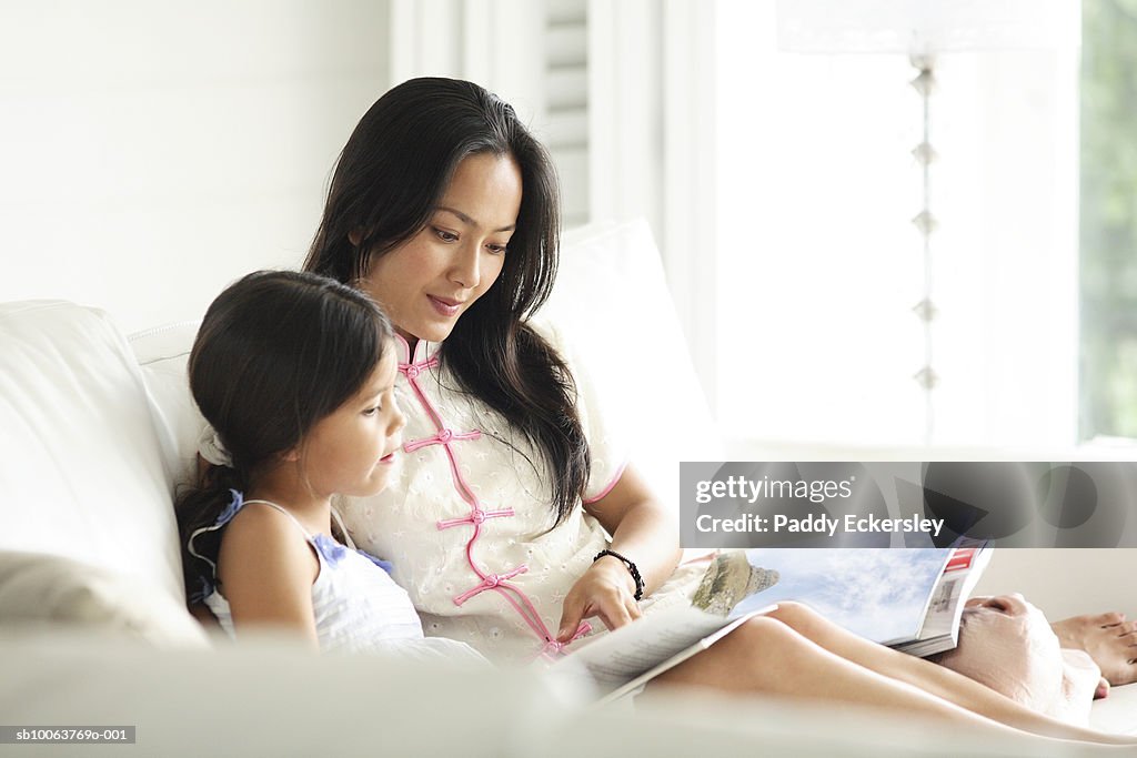 Mother reading book with daughter (8-9) on sofa