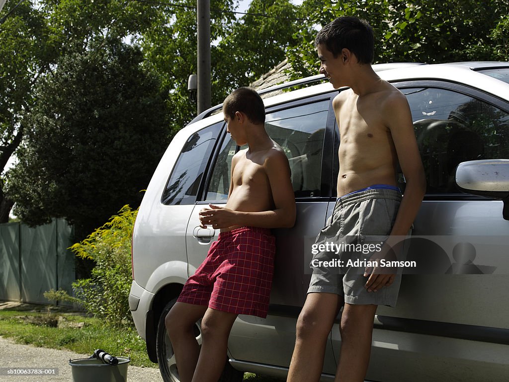 Two boys (10-14) leaning against car