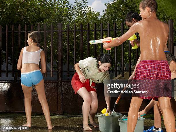 teenage boy and girl (13-15) and children (10-11) playing in water - teen boy shorts stock pictures, royalty-free photos & images