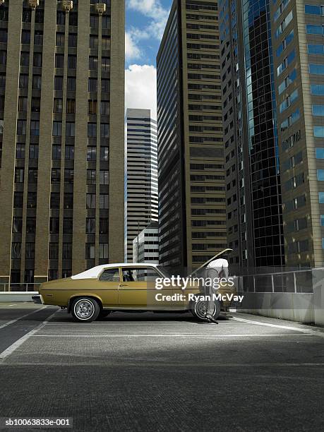 man repairing car on parking lot, looking under bonnet, rear view - old car stock-fotos und bilder