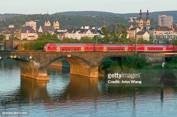 germany, koblenz, train crossing bridge over river with cityscape in background - koblenz stock-fotos und bilder
