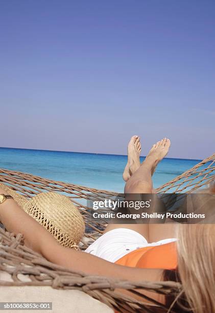 woman relaxing in hammock on beach, over the shoulder view - legs crossed at ankle stock-fotos und bilder