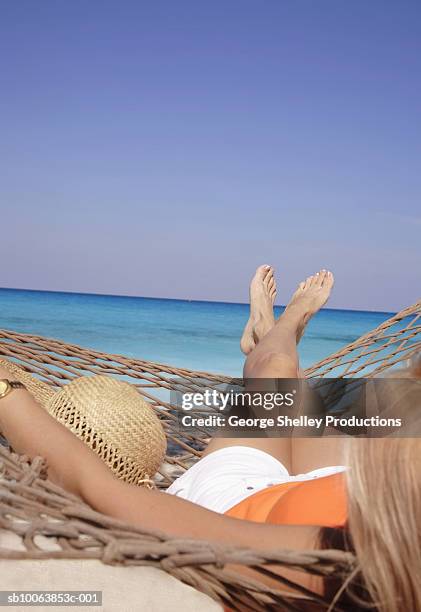 woman relaxing in hammock on beach, over the shoulder view - pés cruzados - fotografias e filmes do acervo