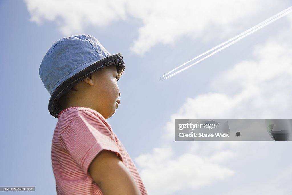 Young boy (2-3) in hat looking at airplane