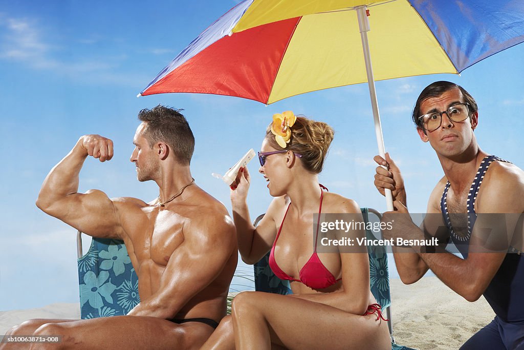 Woman applying moisturiser on man's body, another man holding umbrella