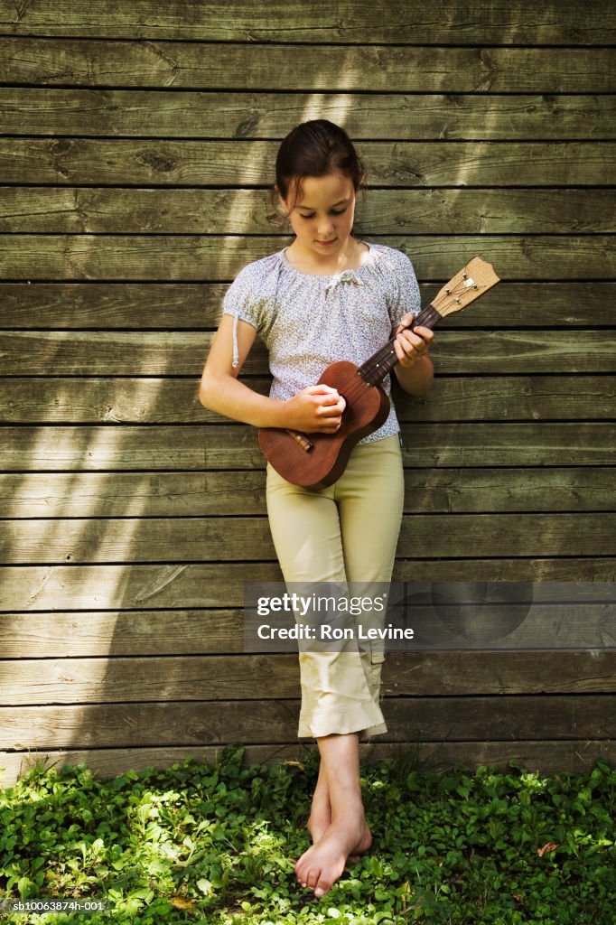 Girl (8-9) leaning against fence, playing ukulele