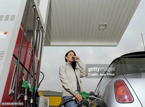 young woman filling car at petrol station drinking from tin, low angle view - drinking soda in car stock pictures, royalty-free photos & images