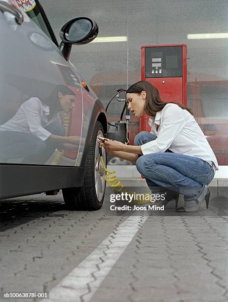 young woman checking air pressure of car tire, side view - inflar fotografías e imágenes de stock