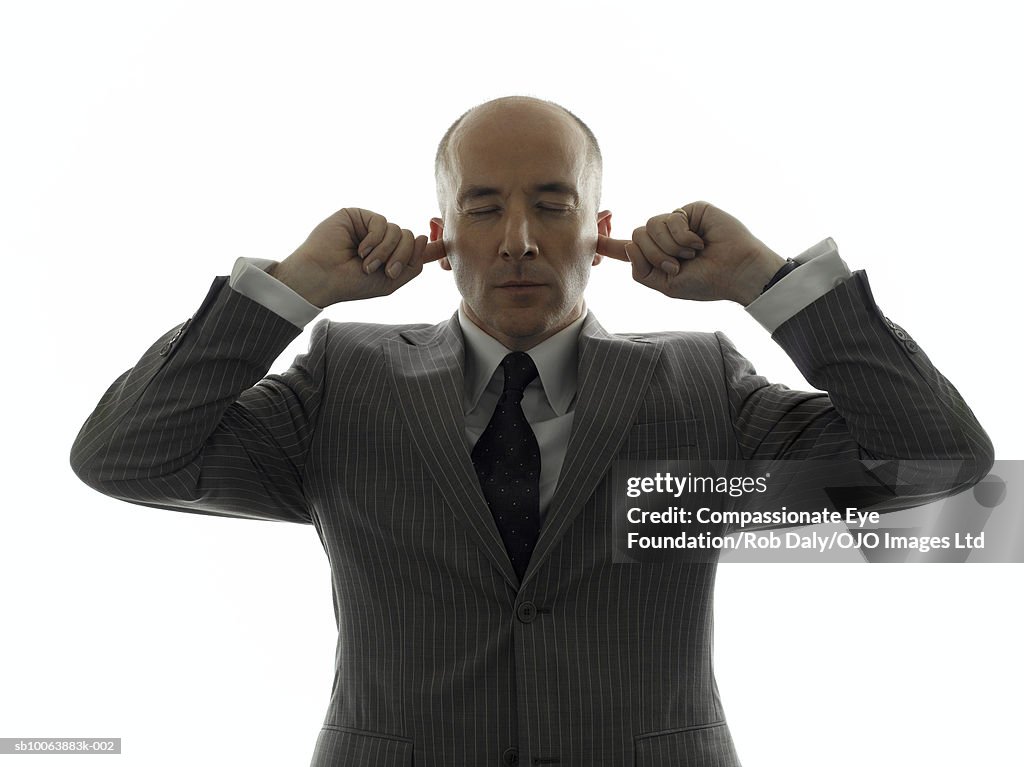 Mature businessman, holding fingers in ears, eyes closed