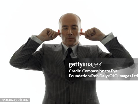 Mature businessman, holding fingers in ears, eyes closed Mature businessman, holding fingers in ears, eyes closed