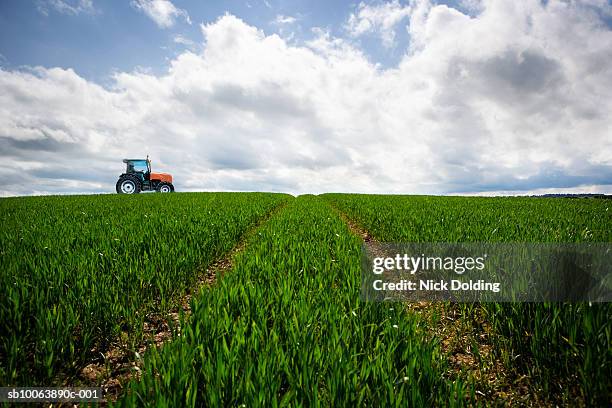 tractor driving along crop field, side view - tractor foto e immagini stock