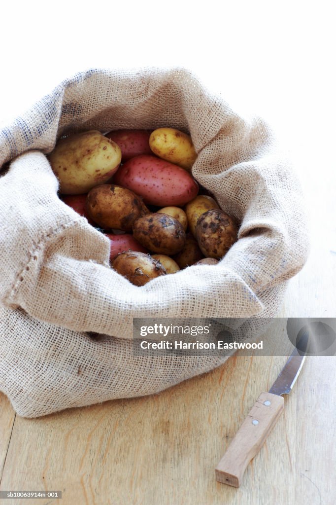 Selection of potatoes in sack on kitchen table with knife