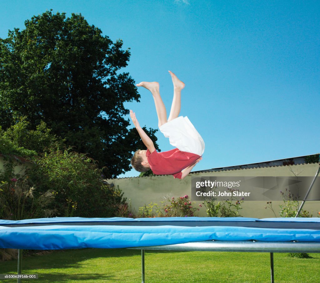 Boy (6-7) jumping on trampoline in garden