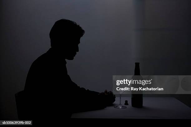 man sitting in dark at table with glass and wine bottle - silhouette sitting stock pictures, royalty-free photos & images