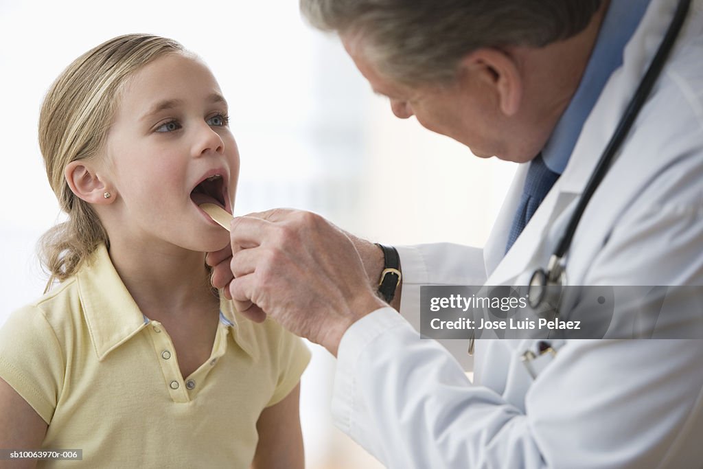 Male doctor examining girls (6-7) throat using tongue depressor
