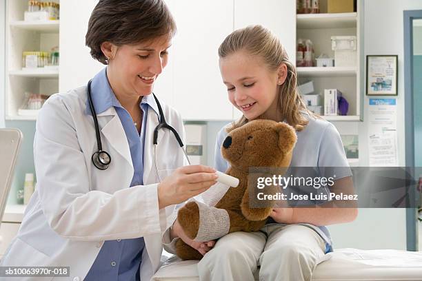 female doctor putting cast on teddy bear's leg, smiling - doctor patient cast stock-fotos und bilder