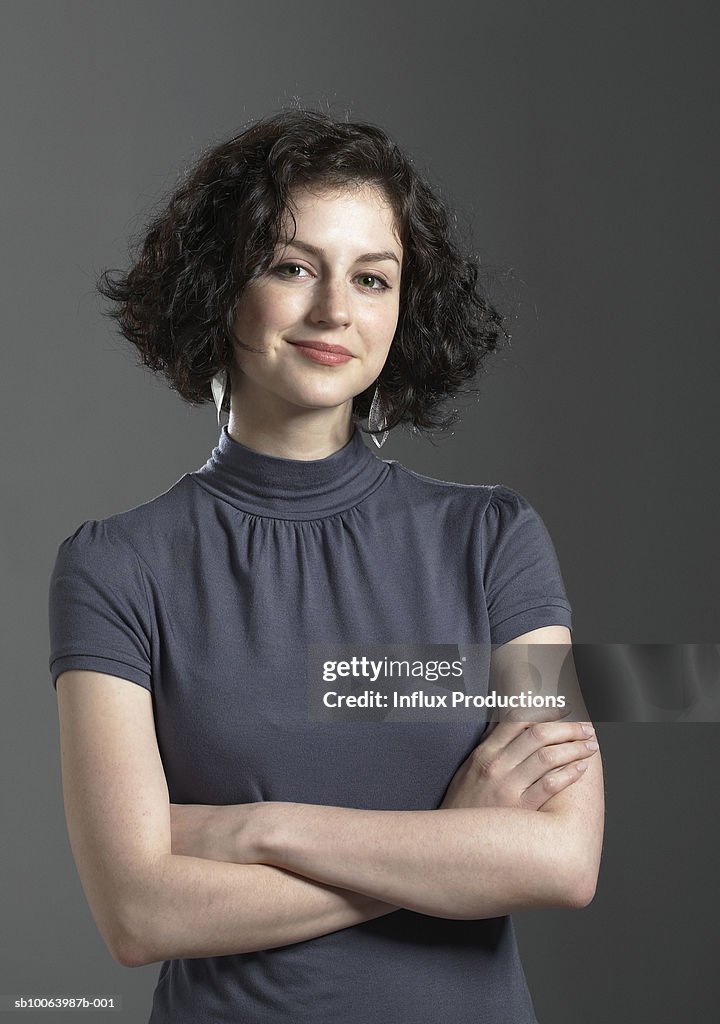 Portrait of young woman with arms crossed, in studio