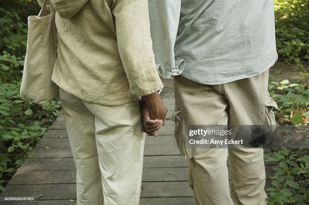 Mature couple on boardwalk, holding hands, mid section