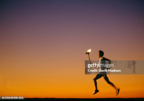 silhouette of man running with torch at sunset, side view - fackel stock-fotos und bilder