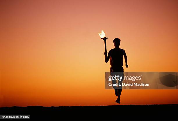 silhouette of man running with torch at sunset - fackel stock-fotos und bilder