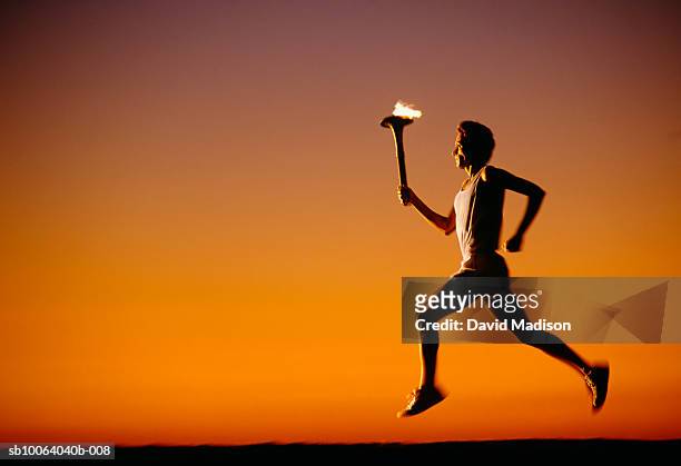silhouette of man running with torch at sunset - laufwettbewerb der männer stock-fotos und bilder